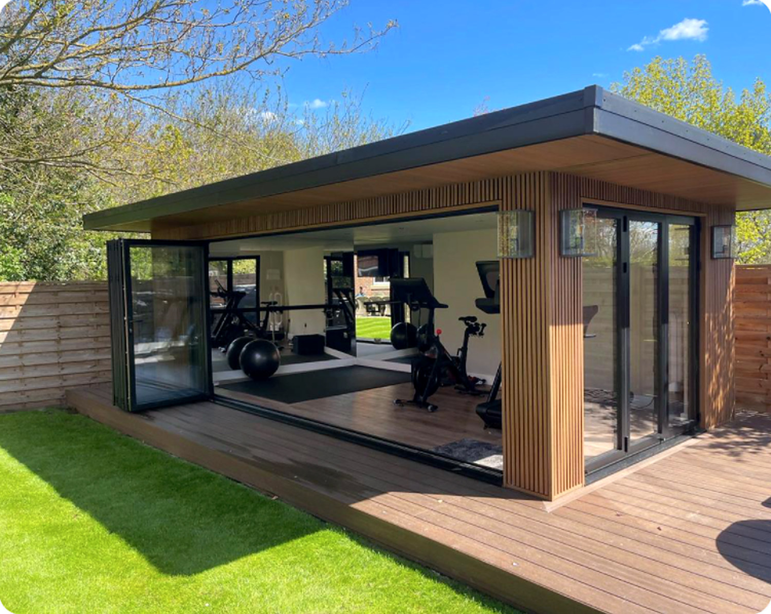 Garden gym with folding glazed doors open onto timber decking, with weights and bikes inside